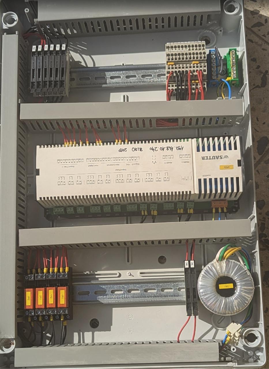 Grey control cabinet with a Sauter controller, terminal blocks, relays and a toroidal transformer.